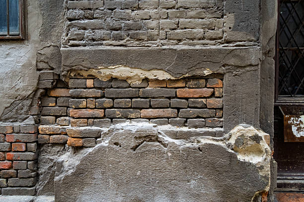A close-up view of an old wall where the plaster has crumbled away, revealing adobe bricks underneath. The rough textures of mud bricks, cracks, and peeling layers emphasize age, decay, and rustic construction methods. The image captures the raw character of traditional architecture and weathered surfaces.