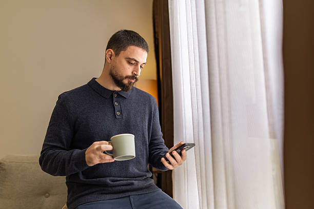 istock Handsome man with beard  using mobile phone and resting near the window at coffee time. 2248620767