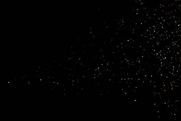 Golden glowing particles sparkling and falling on a black dark background