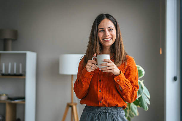 istock Woman smiling holding mug standing by window 2248623256
