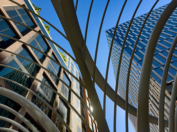 A dynamic upward view of contemporary buildings in Wynwood, Miami, framed by curved metal architectural elements. Reflections on the glass windows and the clear blue sky enhance the clean, modern aesthetic.