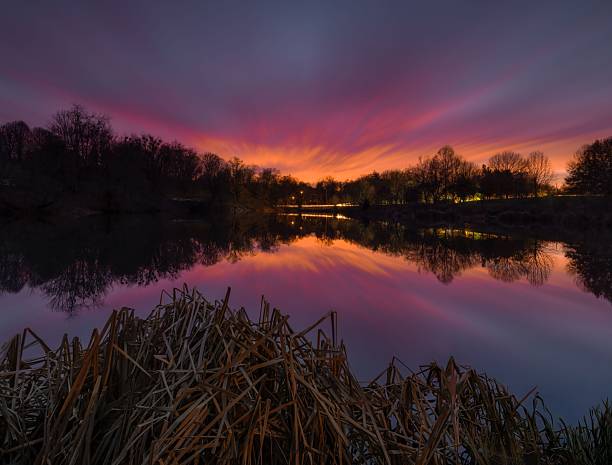 A serene sunset over a tranquil lake with vibrant colors reflecting on the water, surrounded by silhouetted trees.