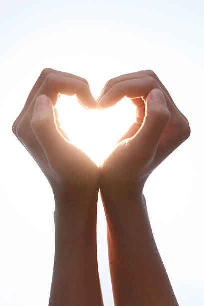 Two hands forming a heart shape against bright sunlight, expressing love, affection, and romantic gesture with warm golden glow.