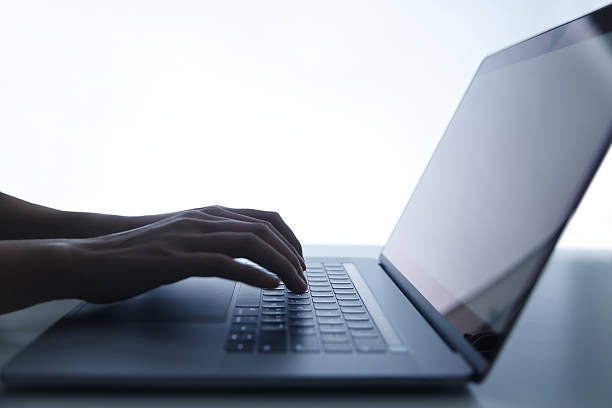 Hands of a woman busy typing on a laptop with a customizable green screen at a desk