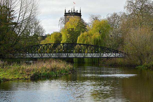 Metal bridge spans calm river, autumn foliage, historic building, peaceful scenic landscape view.. High quality photo