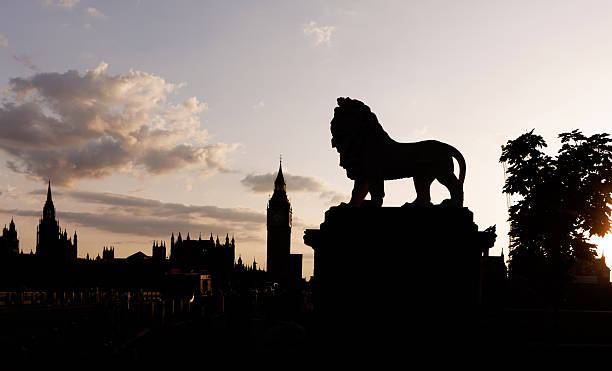 Silhouette of a lion statue overlooking Big Ben and the Westminster skyline at sunset.