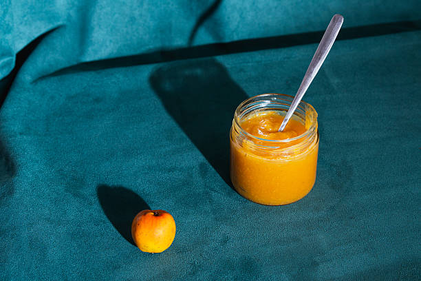 Jar of homemade apple jam with a spoon beside a fresh apple, creating long shadows