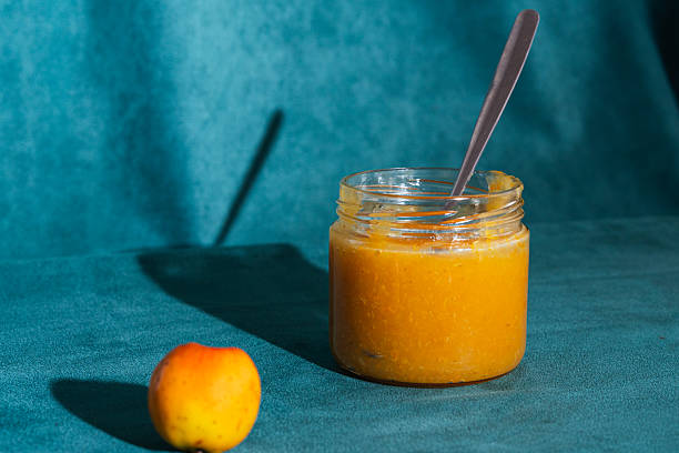 Glass jar of homemade organic apple jam with a spoon and a single apple