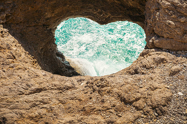 istock Heart-shaped coastal rock window revealing turquoise waves and rugged shoreline below 2248642903