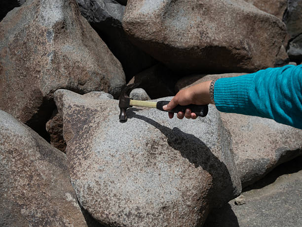 Woman wearing a turquoise sweater tapping a hammer on a ringing rock in the Boulder Mountains in Montana.