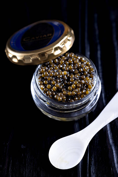 A close-up view of premium caviar in a small glass jar highlights the glossy, golden-black pearls glistening under soft light