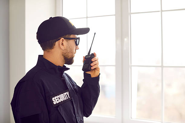 security guard standing inside house, looking out window, and using walkie talkie - beveiliger stockfoto's en -beelden