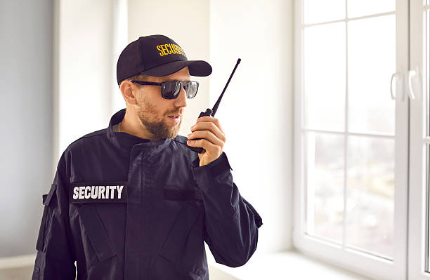 istock Security guard in uniform standing inside house, looking out window, and talking on radio 2248654439