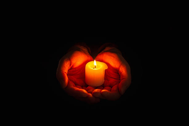 istock Burning candle in the mans hands on a dark background. Religious concept. Selective focus. 2248661838