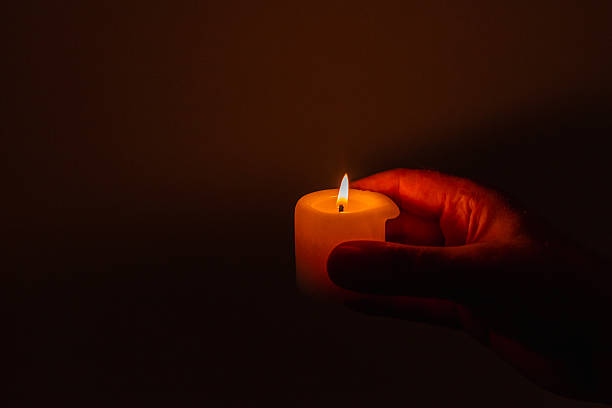 istock Burning candle in the mans hands on a dark background. Religious concept. Selective focus. Side view, copy space. 2248661868