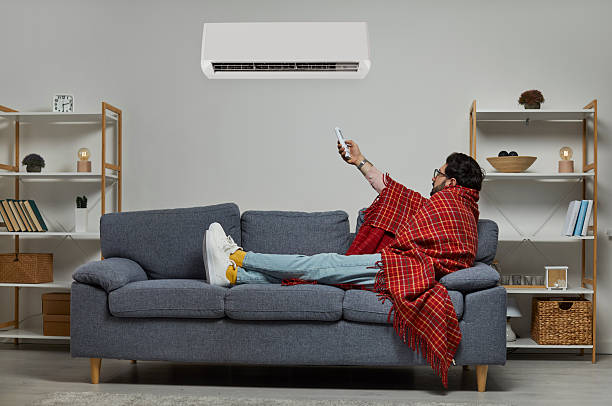istock Young man wrapped in blanket holding air conditioner remote control 2248663279