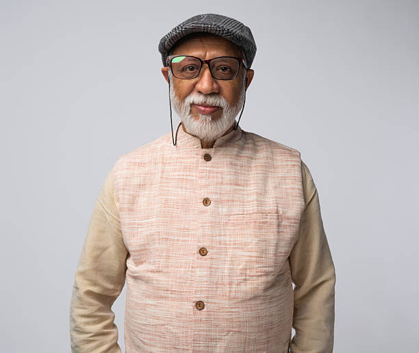 Portrait of happy senior man wearing eyeglasses and cap standing with arms crossed against white background