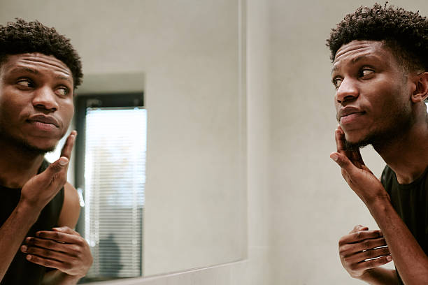 istock Young Adult Black Man Touching Face While Looking at Reflection in Mirror 2248666975