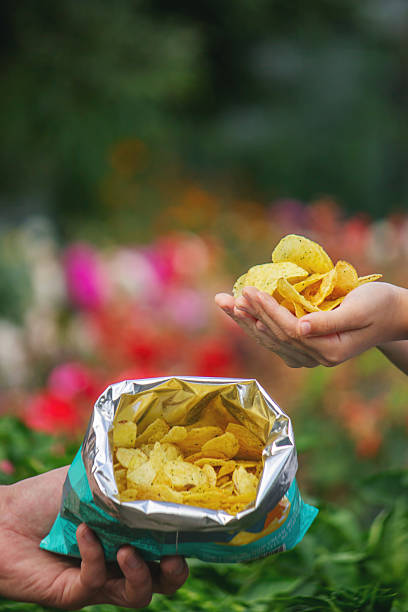istock Child's hands taking a handful of potato chips from an open bag outdoors in summer 2248667149