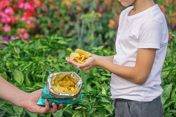 istock Child's hands taking a handful of potato chips from an open bag outdoors in summer 2248667150