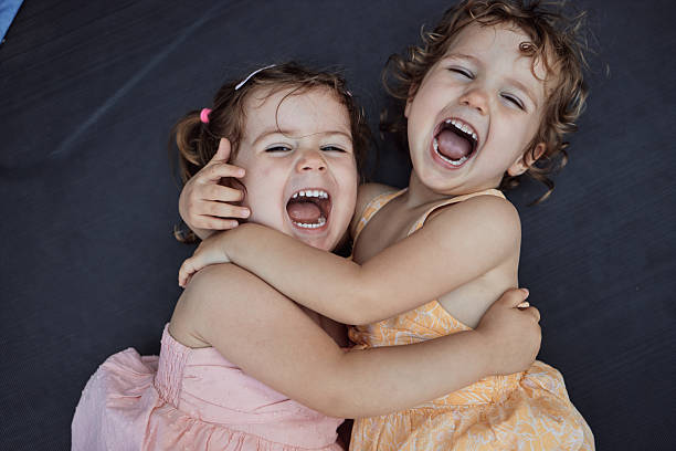 Two young girls embracing, laughing with open mouths, and having fun together outdoors