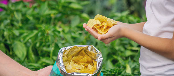 istock Child's hands taking a handful of potato chips from an open bag outdoors in summer 2248667152
