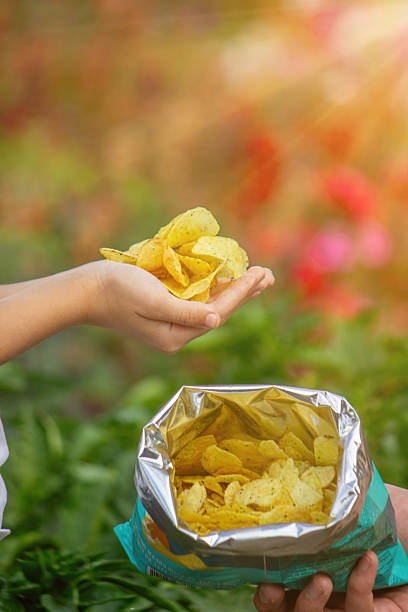 istock Child's hands taking a handful of potato chips from an open bag outdoors in summer 2248667154