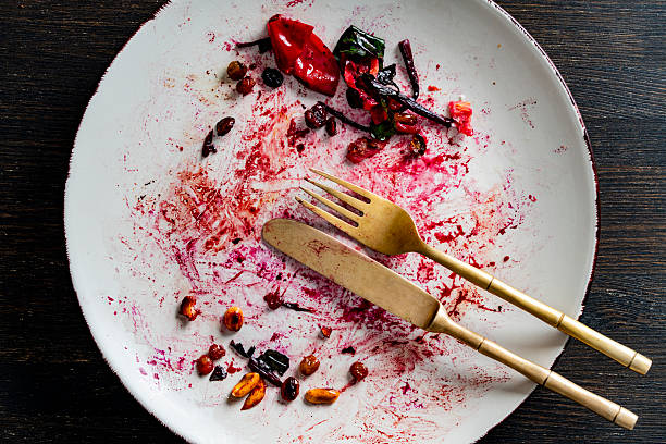 Dirty plate, fork and knife after eating on a wooden table, closeup, top view. End of meal