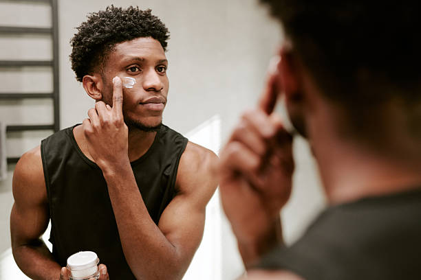 istock Young Adult Black Man Applying Face Cream While Looking in Bathroom Mirror 2248670859