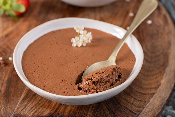 istock Smooth chocolate mousse in a white bowl, a golden spoon lifting a bite, garnished with tiny white flowers, presented on a textured wooden board 2248672810