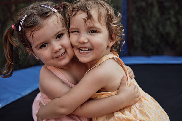 Two cheerful preschool-age girls sharing an affectionate hug, smiling and looking at camera