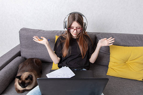 istock Young student engaged in online learning while relaxing on a couch with a cat, showcasing remote education dynamics 2248675665
