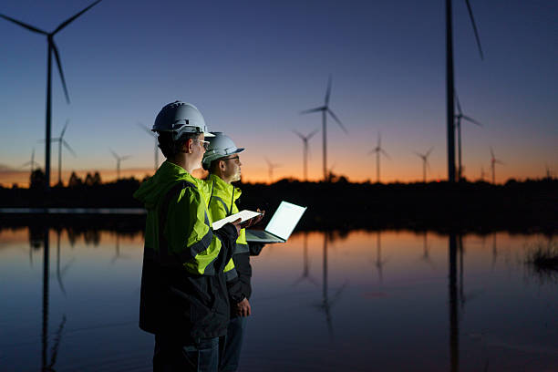 Engineers are checking the operation of a large wind turbine that is working to generate electricity in a wind farm during sunset.