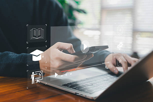 istock Hands using a smartphone and laptop with floating online learning and video playback icons represent e-learning, digital education, online courses, remote study, modern multimedia learning platforms. 2248676069