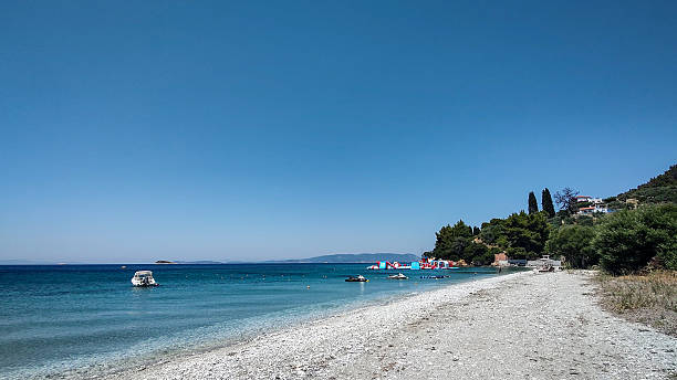 istock Turquoise Seaside with Pebble Beach, Boats, and Hillside Trees on a Clear Summer Day 2248677433