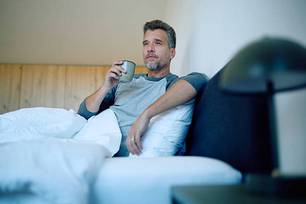 istock Man relaxing in bed, drinking morning coffee and contemplating future, enjoying peaceful routine 2248678942