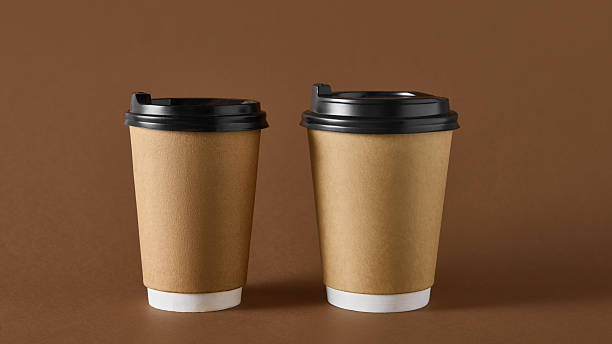 istock Two brown takeaway coffee cups with black lids on brown background for packaging design 2248679717