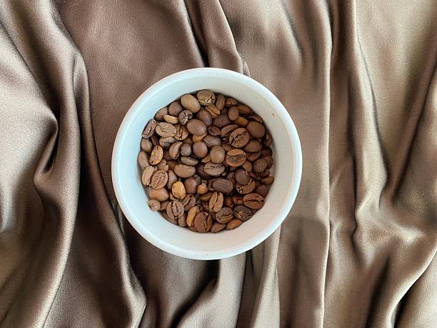 White bowl filled with coffee beans placed on soft brown textile