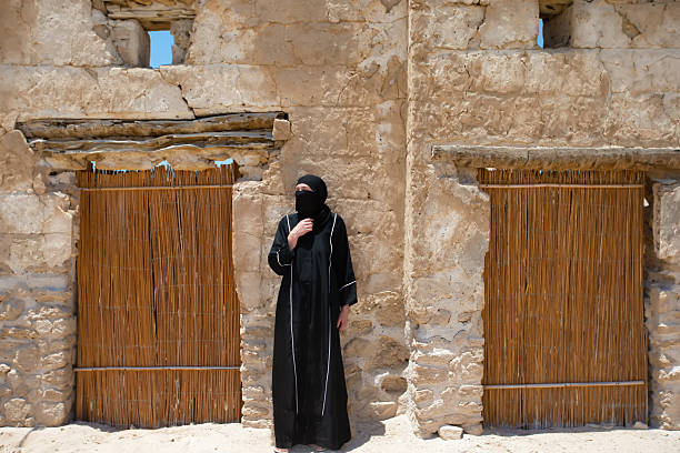 istock Woman in traditional attire stands beside rustic adobe structure in desert at midday 2248680536