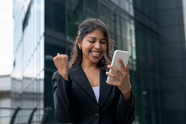 istock Woman celebrating success while using her smartphone outside a modern office building in bright daylight 2248680902