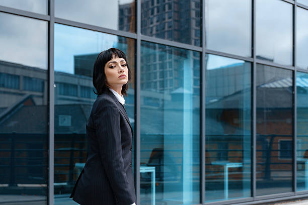 istock Young professional standing confidently in front of modern glass building on a cloudy day 2248682513