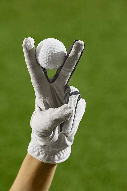 Gloved fingers forming peace sign while holding golf ball on green field. Concept of empowerment, women athletic identity, digital campaign branding, and sports visuals.