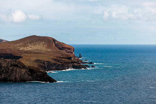 Coastal landscape featuring rugged cliffs meeting the ocean, with waves crashing against the rocky shore under a cloudy sky, evoking a sense of adventure and natural beauty