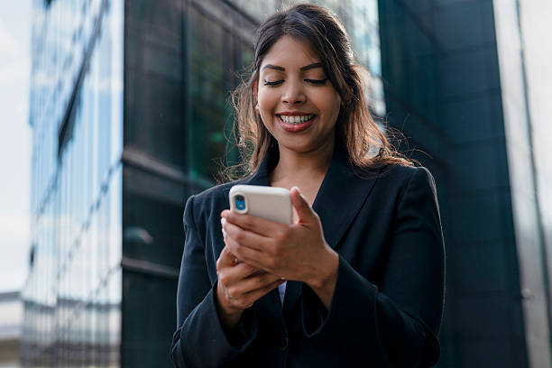 istock Business professional smiles while using smartphone outside modern office building during daylight 2248687073