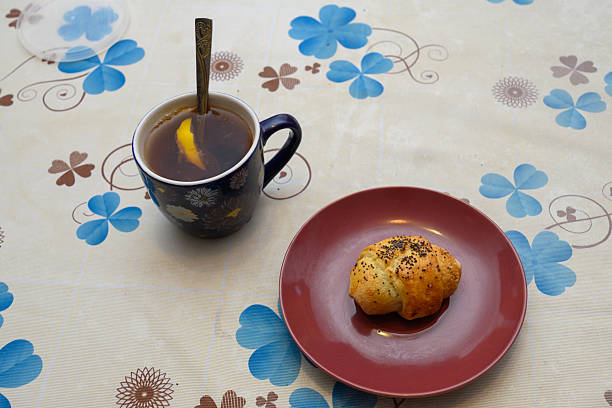 delicious breakfast consists of blue mug of hot tea with lemon slice and fresh bagel on red plate standing on floral tablecloth in kitchen for pleasant start of day