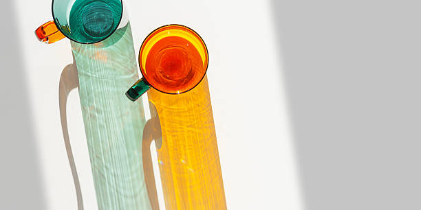 istock Orange and green Glass Mugs with bright sunlight Shadows, banner with transparent cup casting dynamic, vibrant lights reflections and shadows on light white, creative aesthetic top view, minimal 2248698062
