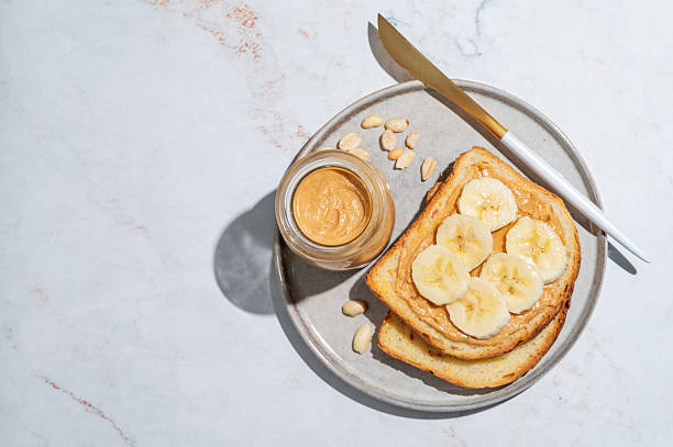 istock Peanut butter toast and banana on a plate on a marble background with nuts 2248698977