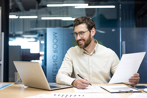 istock Young office man working at a desk with documents, talking on a video call on a laptop 2248700704