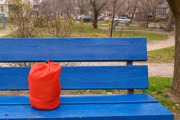 a bright red fabric sack or cover bag is standing on a blue wooden bench in the courtyard of a residential building, personal items