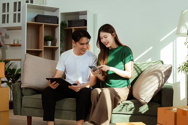 istock Young couple relaxing sitting on the sofa using the computer laptop around cardboard boxes, very happy moving to a new house. 2248704801